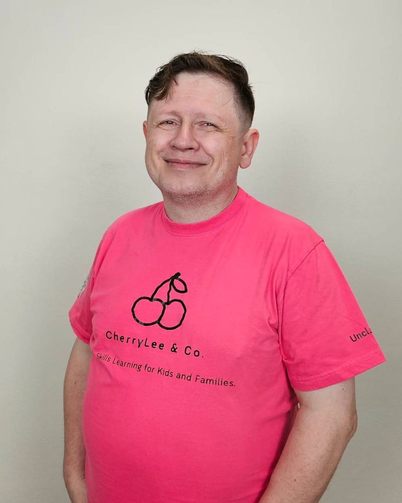 อังเคิลลี ยิ้มอย่างเป็นกันเองในเสื้อยืดสีชมพูลายโลโก้ CherryLee & Co.